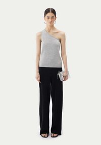 Grå topp med en axel i stickad tyg, kombinerad med svarta, vida ribbade byxor. Tillbehör inkluderar en liten silverclutch och sandaler med remmar.