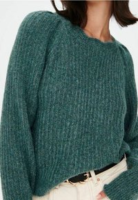 Pull en tricot texturé teal avec un design côtelé et une coupe décontractée, doté de manches longues et d'un col rond. Associé à une ceinture de couleur claire.