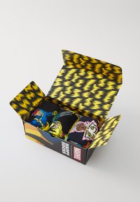 Trīs melnu zeķu pāri ar krāsainu Marvel varoņu dizainu, iepakoti grafiskā kastē ar dzelteniem zigzaga akcentiem.