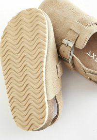 Sandales en daim beige avec une semelle en caoutchouc texturée ondulée, boucle métallique réglable et design à dos ouvert.