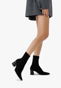 Czarne botki za kostkę wykonane z miękkiego aksamitu o luźnym fasonie, w szpic i na grubym obcasie. Odpowiednie do różnych stylizacji.