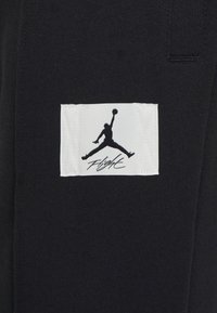 Schwarzer Stoff mit glatter Textur zeigt ein weißes rechteckiges Etikett mit einem schwarzen Silhouettenlogo und dem Text "Flight" darunter.