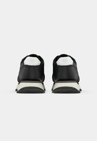 Svart sneakers med en glatt skinnoverdel, hvite detaljer ved hælen, avrundet design og en strukturert gummisåle.