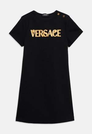Black short-sleeve dress with gold "VERSACE" lettering across chest and two gold decorative buttons on left shoulder.