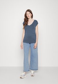 Top azul escuro de manga curta com decote em V, combinado com jeans de perna larga azul claro e sapatilhas bege com detalhes em cinza e branco.