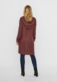 Długi, głęboki bordowy kardigan z kapturem, ze ściągaczami na mankietach i u dołu, noszony na ciemnych jeansach i czarnych botkach za kostkę.