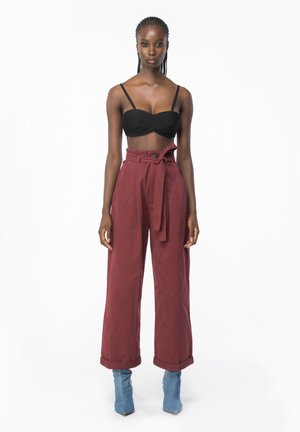 Top noir court avec de fines bretelles associé à un pantalon large bourgogne taille haute avec une ceinture à nouer. Bottines bleu pointues.