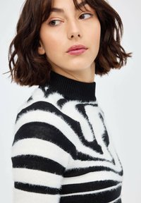 Suéter de rayas blanco y negro con un alto cuello de canalé. Textura suave y esponjosa con rayas gruesas alternas y un diseño ajustado.