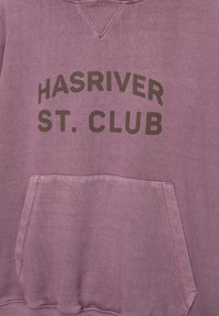 Sweatshirt violet avec poche avant, portant le texte "HASRIVER ST. CLUB" en marron foncé. Texture douce et design décontracté.