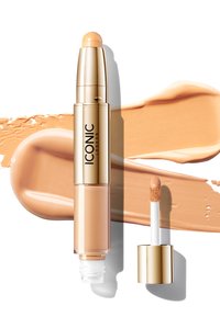 Correttore liquido beige in un tubo dorato, dotato di una morbida punta applicatrice. Strisce di fondotinta circostanti in una tonalità corrispondente.