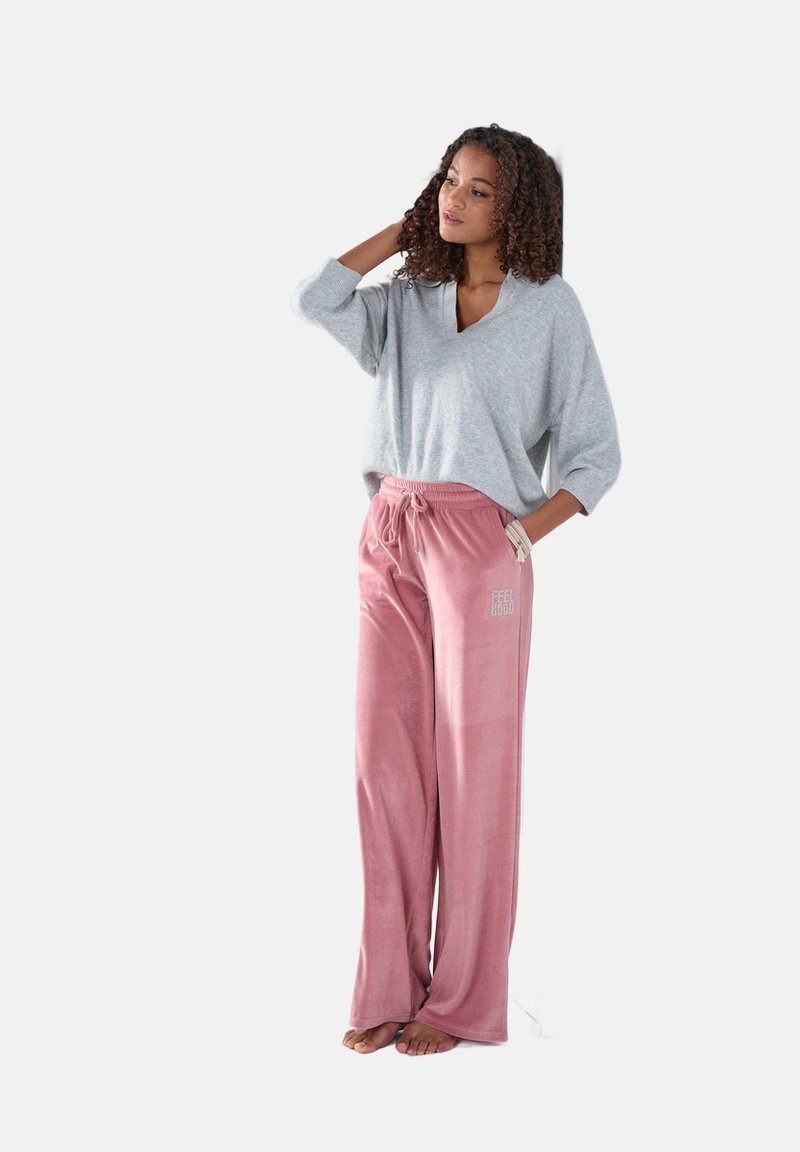Grijze V-hals trui gecombineerd met roze sweatpants met trekkoord en de tekst "FEEL GOOD". Zachte textuur met een relaxte pasvorm en wijde pijpen.