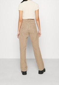 Ljusbeige kordbyxor med hög midja, med bakfickor och raka ben, tillsammans med en kortärmad krämfärgad topp.