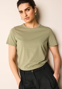 Camiseta de manga corta en verde oliva, hecha de una tela suave con un escote redondo. Combinada con pantalones negros de cintura alta que cuentan con bolsillos laterales.