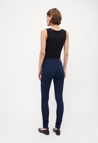 Navy blue elastiske leggings med en tettsittende design og baklommer, kombinert med en svart ermeløs topp. Glatt stoff og smalere ben.