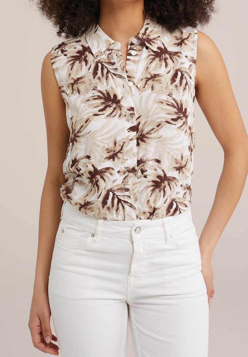 Haut sans manches à col avec boutons, imprimé feuilles de palmier marron et beige, porté avec un pantalon blanc taille haute.