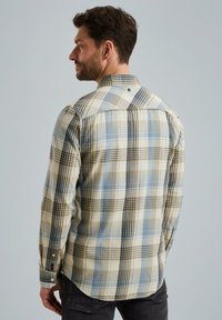 Chemise à carreaux beige, bleue et noire. Elle présente des manches longues, un col classique et un ourlet arrondi. Tissu texturé.