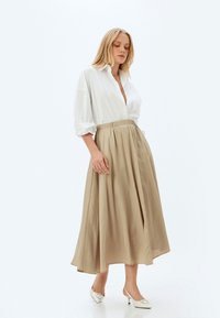 Chemise blanche à col et jupe midi beige avec une taille élastique, présentant un design fluide et une texture de tissu lisse. Chaussures à talons élégantes.