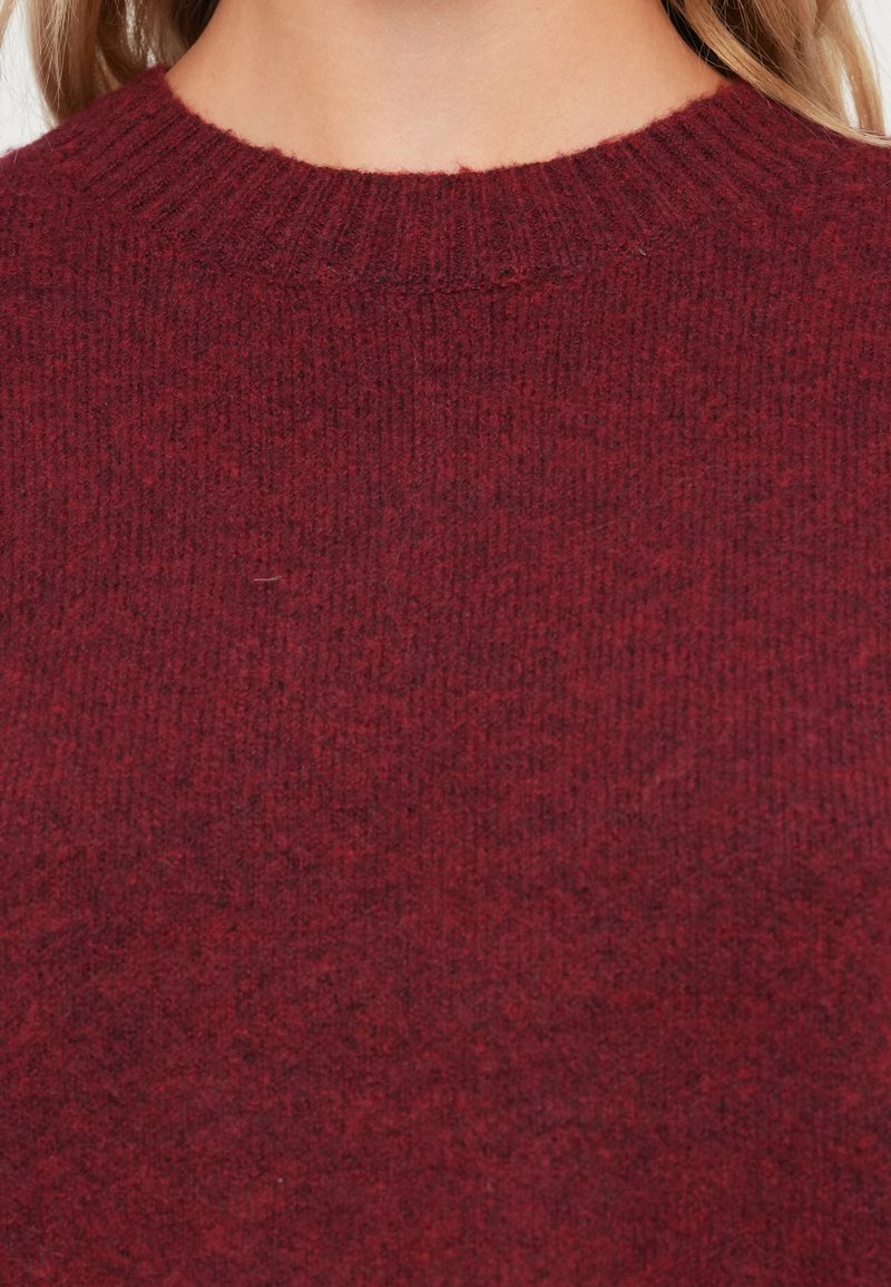 Suéter burdeos con cuello redondo acanalado y tejido texturizado, con un acabado suave y sutiles variaciones de color en todo su diseño.