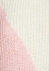 Stickad tyg i vitt och mjukt rosa, med ett diagonalt delat mönster och en slät textur samt svag ribbdetalj.