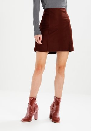 Kobieta ubrana w ciemnoczerwoną mini spódnicę, szary top z długim rękawem oraz pasujące ciemnoczerwone aksamitne botki na słupku.