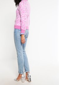 Pull en tricot à imprimé léopard rose, jeans bleu clair à revers, et chaussures à talons aiguilles argentées. Motif texturé sur le pull.