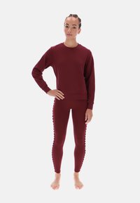 Bordowy komplet z bluzy i legginsów. Bluza ma długie rękawy i okrągły dekolt. Legginsy zdobią faliste detale po bokach i mają dopasowany design.