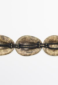 Cintura color bronzo con sezioni ovali metalliche, collegate da cordini neri con accenti dorati, che mostrano il nome del marchio "Massimo Dutti."