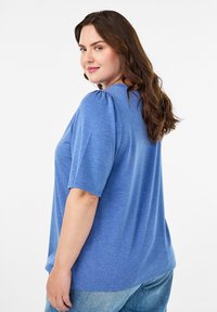 Niebieska, krótko rękawowa bluzka o luźnym kroju, miękkiej strukturze i subtelnie bufiastych ramionach. W połączeniu z jasnoniebieskimi dżinsami.