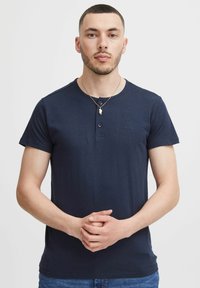 Marineblå kortærmet t-shirt med rund halsudskæring, to-knaps knaplukning og et diskret logo på brystet. Blødt og glat stof.