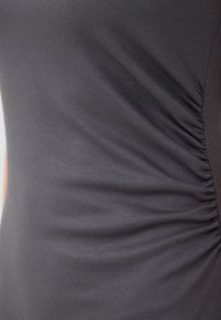 Haut gris ajusté en tissu doux et extensible. Présente une texture froncée sur le côté, créant un léger effet ruissé. Design simple et sans couture.