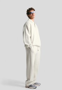 Light grey, oversized fleece sweatshirt with a half-zip and matching sweatpants. Worn with grey sneakers and sunglasses.