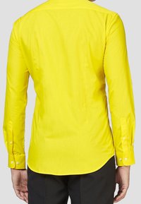 Camisa de manga larga de algodón en color amarillo brillante. Presenta un canesú en la espalda, un dobladillo curvado y puños con botones. Textura suave sin patrones.