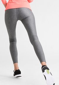 Leggings grigi con un design aderente, superficie testurizzata e dettagli cuciti. Indossati con sneakers nere con suola bianca.