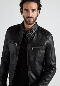 Zwarte leren motorjack met staande kraag, ritszakken en gewatteerde schouderdetails. Gladde textuur met een klassiek ontwerp.