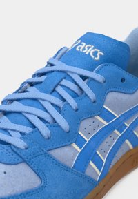 Zapatillas de ante azul con acentos blancos, superficie texturizada y cordones planos. Incluyen marca y detalles en azul claro contrastantes. Suela de goma.