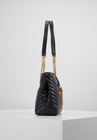 Mustat nahkalaukku, jossa on päälystetty kankainen muotoilu. Varustettu pitkillä nahka- ja kultaketjuilla, joissa on tupsu ja kapeneva muoto.