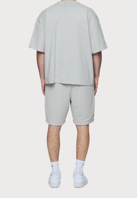 Camiseta de corte oversize en gris claro con mangas cortas, combinada con pantalones cortos de textura en gris claro y zapatillas blancas, mostrando un ajuste relajado.