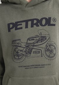 Sudadera verde oliva con un gráfico azul oscuro de una motocicleta, con el texto "PETROL" y detalles de ubicación impresos debajo.