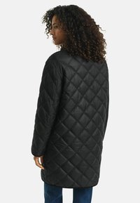 Zwarte gewatteerde jas met een lang model, voorzien van een diamanten patroon, verlaagde schouders en een gladde textuur.