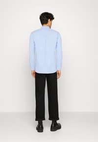 Camicia azzurra a maniche lunghe con colletto a fascia, dotata di una piega sul retro. Indossata con pantaloni neri a gamba larga e stivali neri spessi.