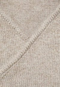Pull en tricot beige avec un design en V, présentant une légère texture et des variations de fil naturelles, mettant en valeur une structure douce et uniforme.
