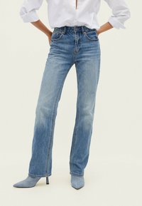 Jeans azzurri chiari a vita alta con una vestibilità dritta. Presentano cinque tasche, leggeri effetti di scoloritura e dettagli di cucitura. Abbinati a décolleté azzurri chiari con punta.