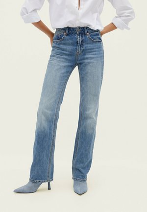 Jeans bleu clair taille haute avec une coupe droite. Présente cinq poches, un léger dégradé et des détails de couture. Associée à des talons aiguilles bleu clair.