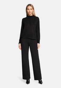 Czarny dziergany sweter z teksturowanym wzorem, okrągłym dekoltem i długimi rękawami, zestawiony z czarnymi, szerokimi spodniami o wysokim stanie oraz czarnymi botkami za kostkę.