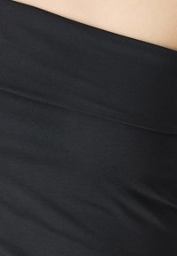 Černá elastická tkanina s hladkou strukturou, obsahující široký pas. Design je přiléhavý, zdůrazňující pohodlí a snadnost nošení.