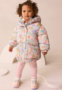 Padded coat with a pastel pattern of animals and shapes, gray base, large pockets, and a hood; paired with pink pants and colorful sneakers.