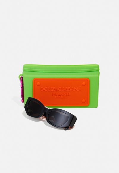 Bolsa de silicone verde com um emblema laranja e hardware rosa, acompanhada de óculos de sol pretos com uma armação larga e lentes escuras.
