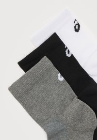 Τρία διπλωμένα καλτσάκια μεσαίου μήκους σε γκρι, μαύρο και άσπρο, το καθένα με ένα μερικό λευκό λογότυπο κοντά στη μανσέτα, παρουσιάζονται σε λευκό φόντο.