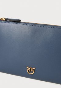 Borsa in pelle blu con una zip dorata, con un dettaglio logo che rappresenta due uccelli. Texture liscia e design strutturato.