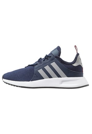 Granatowy sneaker Adidas z szarymi paskami, białą podeszwą, czarnymi sznurówkami i czerwonym zaczepem na pięcie, pokazany z boku na białym tle.